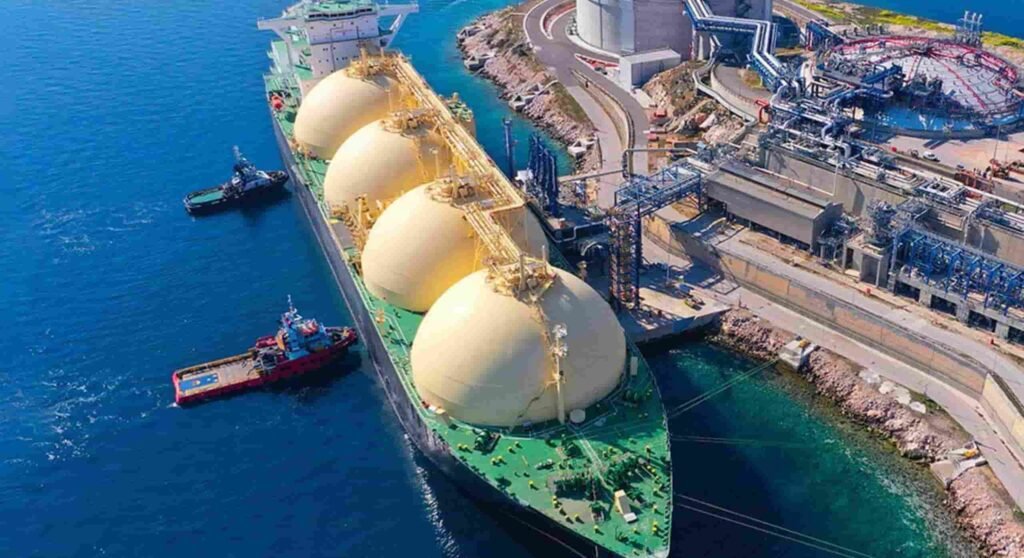 Large cargo vessel docked at an industrial port with storage tanks and pipelines, representing global logistics, shipping operations, and supply chain infrastructure.