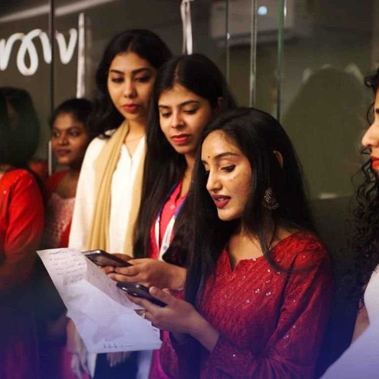 Students gathered indoors, reading from a paper and using a phone during a cultural or group activity in the best logistics institute in kerala, highlighting student participation and collaboration.